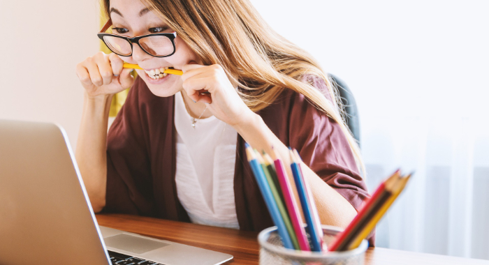 Frustrated asian woman biting pencil while looking at laptop